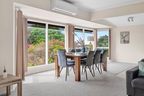 A dining area with a large table and chairs, a lamp, and a view of greenery outside.