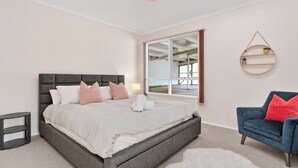 Ein Schlafzimmer mit einem Bett, einem Sessel, einem Nachttisch, einer Lampe, einem Spiegel und Blick ins Freie.