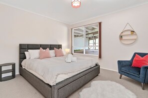 Une chambre à coucher comprenant un lit, une chaise, une table de chevet, une lampe, un miroir et une vue sur l’extérieur.