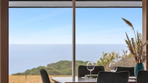 Ein Esstisch mit Stühlen, eine Vase mit Pflanzen und zwei Weingläsern, mit Blick auf die Küste.