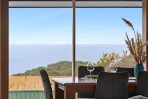 Une table à manger avec des chaises, un vase avec des plantes et deux verres à vin, le tout placé de manière à offrir une vue sur la côte.