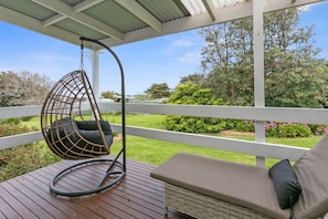 A covered outdoor seating area with a hanging chair and a cushioned bench.