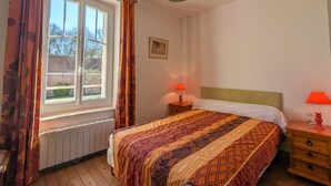 Een slaapkamer met een bed, een nachtkastje, een raam met gordijnen, een radiator en een hanglamp.