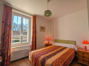 Ein Schlafzimmer mit Bett, Fenster mit Vorhängen, einer Nachttischlampe und einem Heizkörper.