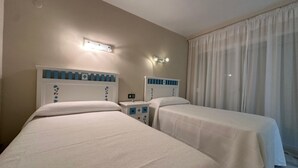Ein Hotelzimmer mit zwei Betten, einem Nachttisch, einer Lampe und einem Fenster mit Vorhängen.