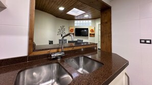 Eine Küche mit doppelter Spüle, Holzboden und einem an der Wand befestigten Flachbildfernseher.