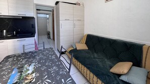 Un ambiente compatto con angolo cottura, divano con cuscini, tavolo da pranzo e un poster appeso al muro.