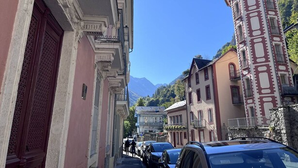 Un vicolo stretto con edifici storici, tra cui una torre con un tetto a punta e un palazzo con una porta rossa.