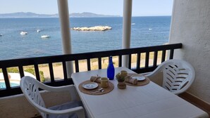 A balcony with a table set for two, overlooking a body of water with boats and a rocky outcrop. - Cozy apartment with terrace and pool 50m from the beach (L'Escala)