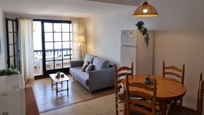 A compact living space with a sofa, dining table, chairs, a refrigerator, and a hanging plant. - Cozy apartment with terrace and pool 50m from the beach (L'Escala)