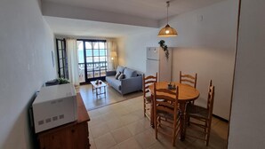 A compact living space with a kitchenette, a dining area, a sofa, and a view of the sea through large windows. - Cozy apartment with terrace and pool 50m from the beach (L'Escala)