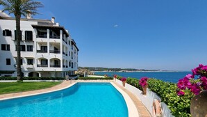 A swimming pool with a view of the sea, a white building with balconies, and pink flowers along the poolside. - Cozy apartment with terrace and pool 50m from the beach (L'Escala)