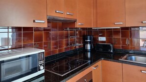 Una cocina con armarios marrones, microondas, estufa, cafetera y tostadora.