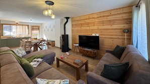 A modern living room with a large TV, wooden panel walls, a fireplace, and a dining area with a view. - New chalet in Vars, 10 guests, 300m from slopes (Vars)