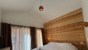 A hotel room with a wooden headboard, a large bed with white linens, a bedside lamp, and a view through sheer curtains. - New chalet in Vars, 10 guests, 300m from slopes (Vars)