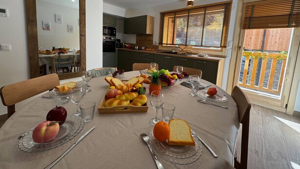 A dining area with a table set for two, featuring a fruit platter, bread, and glasses. - New chalet in Vars, 10 guests, 300m from slopes (Vars)