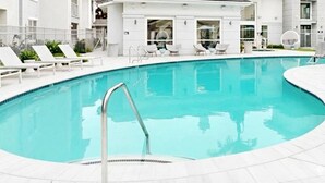 En modern inomhuspool med kristallklart blått vatten, omgiven av vita solstolar och en vit byggnad med stora fönster.