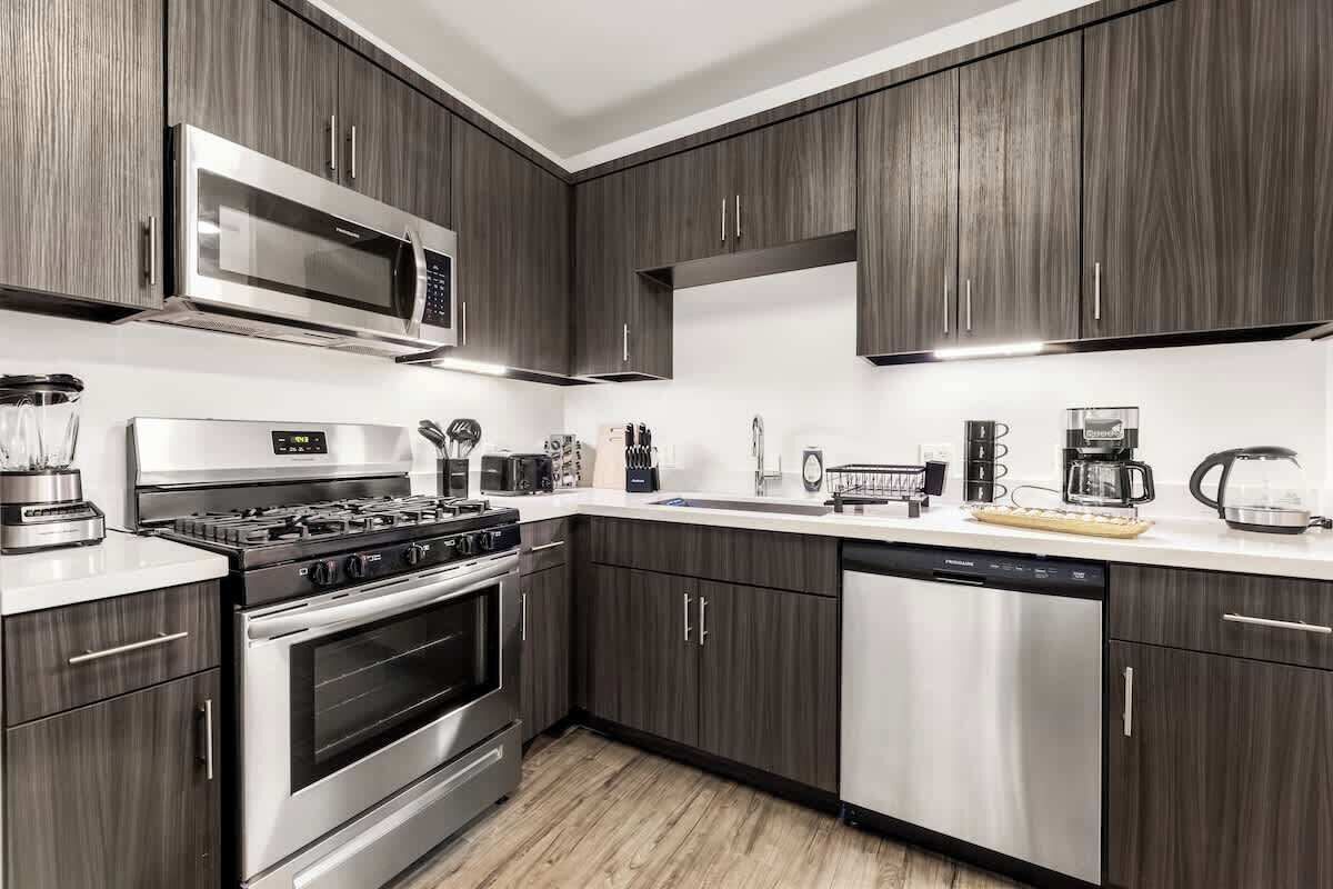 A modern kitchen with dark wood cabinets, stainless steel appliances, and a white countertop.
