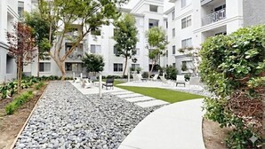 Ett modernt bostadskomplex med utomhusområden med sittplatser, en vacker trädgård och en gångstig.
