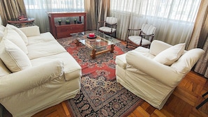 Un salon avec deux canapés blancs, une table basse en verre et un tapis à motifs.