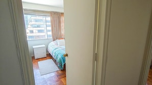 Une chambre avec un plancher en bois, un lit recouvert d’une couvre-lit à rayures, une table de chevet et une fenêtre avec des rideaux.