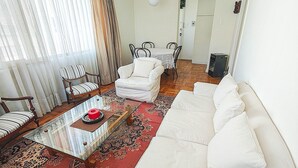 Un salon avec un canapé blanc, une table basse en verre, un tapis à motifs et un coin repas comprenant une table et des chaises.