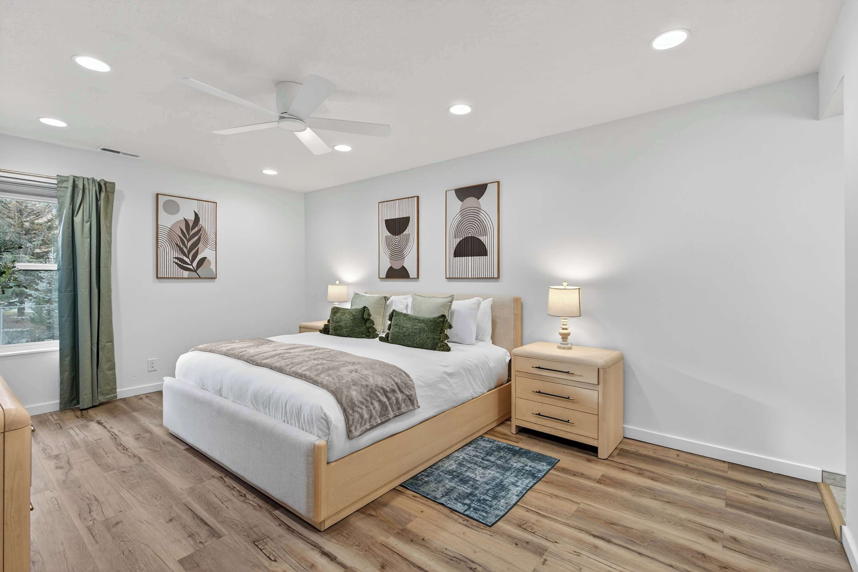 Une chambre à coucher moderne, avec un lit, des tables de chevet, un ventilateur de plafond et des œuvres d’art accrochées aux murs.