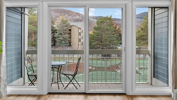 A balcony with a view of a tennis court and surrounding trees. - Walk to PCMR • Chic Top-Floor Mountain Condo (Park City)