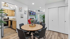 A modern kitchen with wooden cabinets, a dining area with a round table and chairs, and a TV mounted on the wall. - Walk to PCMR • Chic Top-Floor Mountain Condo (Park City)