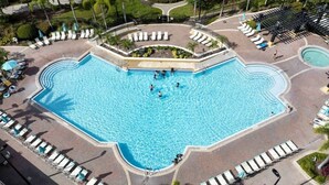 Une grande piscine en forme de cœur, entourée de chaises longues et de parasols, avec une petite piscine et un espace paysager à proximité.