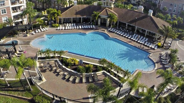 A large swimming pool surrounded by lounge chairs and palm trees, with multi-story buildings in the background. - Last Minute Disney Getaway! Luxury Condo with Private Balcony. Book Now! #114247 (Orlando)