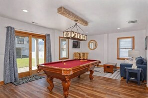 A spacious room with a pool table, a blue sofa, and a wooden ceiling beam. - 4 Bedroom Family-Friendly: 2 King Suites: Walk to Beach, Hot Tub & Game Room! (Kill Devil Hills)
