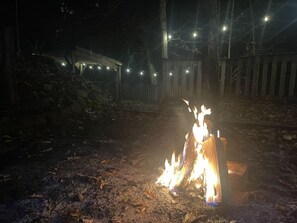 Ein Lagerfeuer mit einer Holzhütte im Hintergrund.