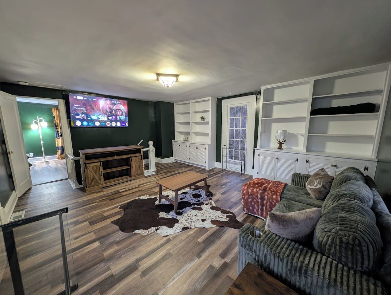 Un salon avec un plancher en bois, un tapis en peau de vache, un canapé et un téléviseur fixé au mur.