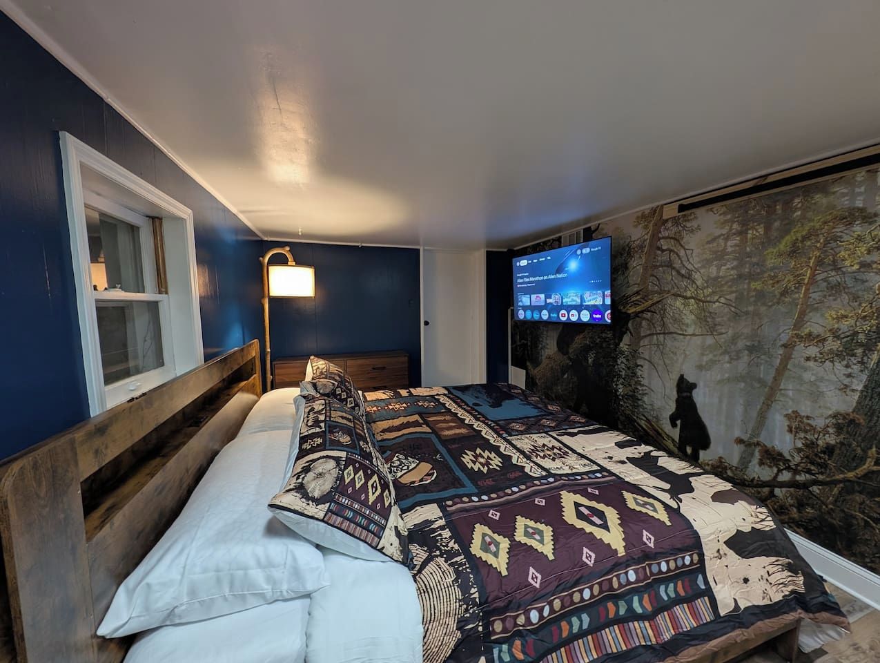Un dormitorio con una cama, televisor montado y un mural en la pared.