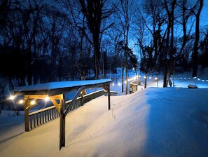 A snow-covered outdoor area with a wooden bench and a railing, surrounded by trees. - Wooden Oasis minutes from Burdette & USI (Evansville)