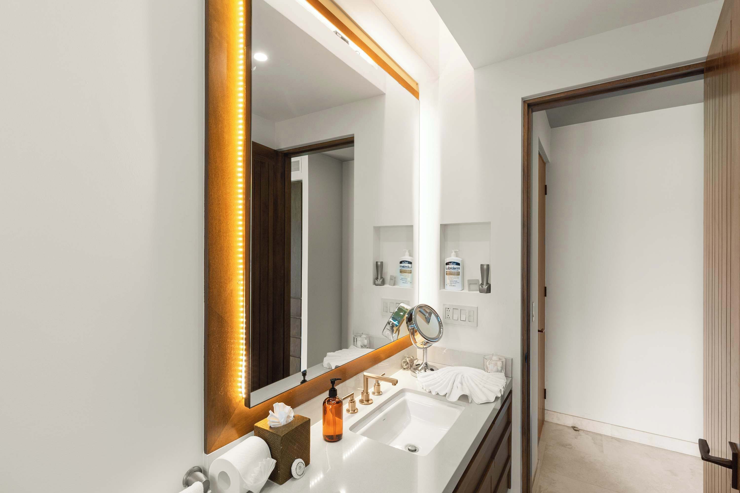 A modern bathroom with a large mirror, a white sink, and a wooden door.