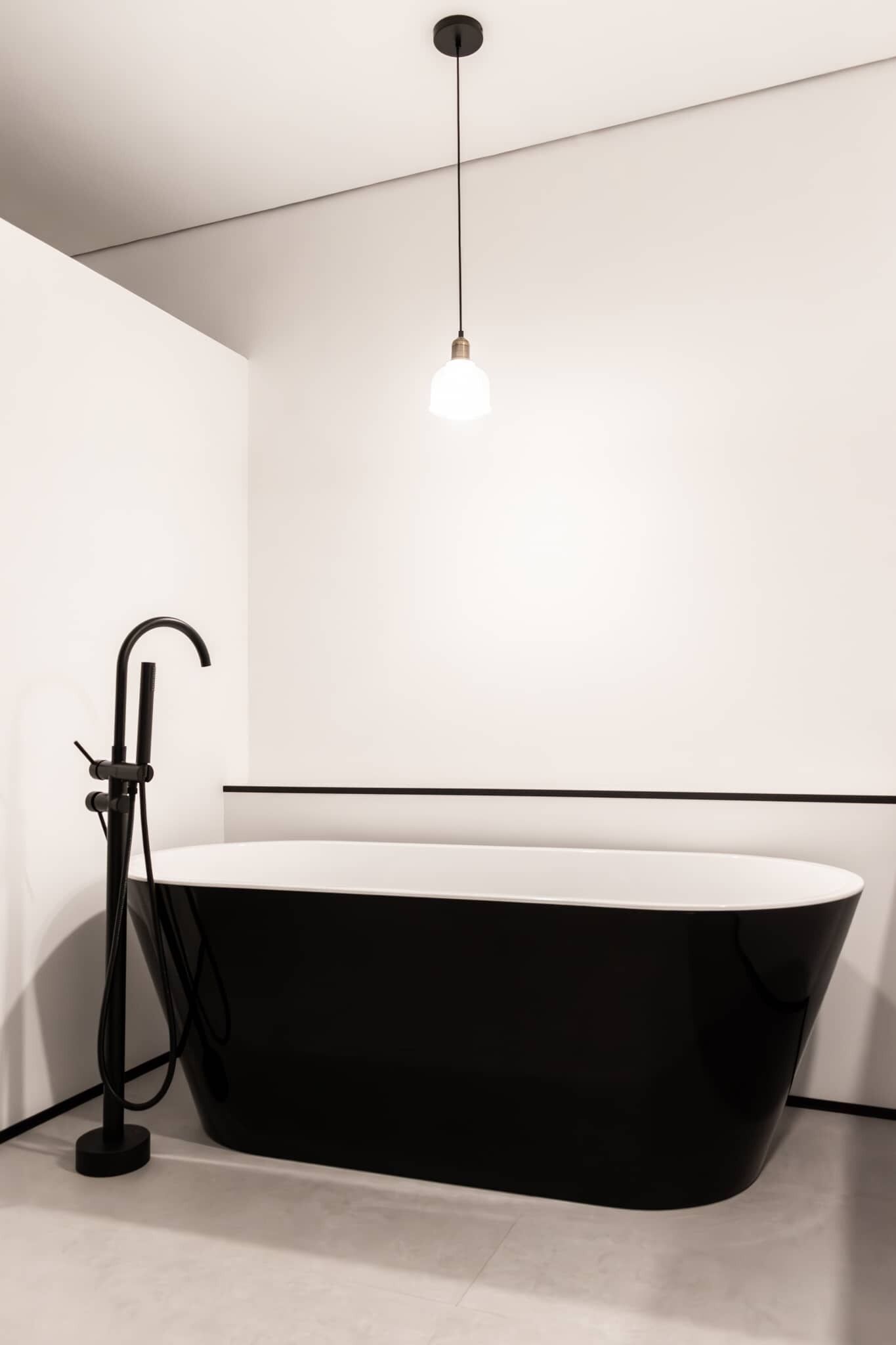 Um banheiro moderno com uma banheira independente, uma torneira preta e uma luminária pendente.