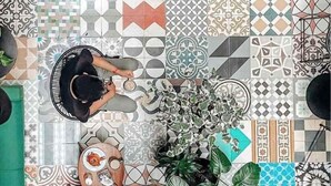 A top-down view of a room with a variety of patterned tiles on the floor, a wooden table with a plate and a cup, and several potted plants. - Puerta roja Increible ubicacion en condesa suite (Ciudad de México)