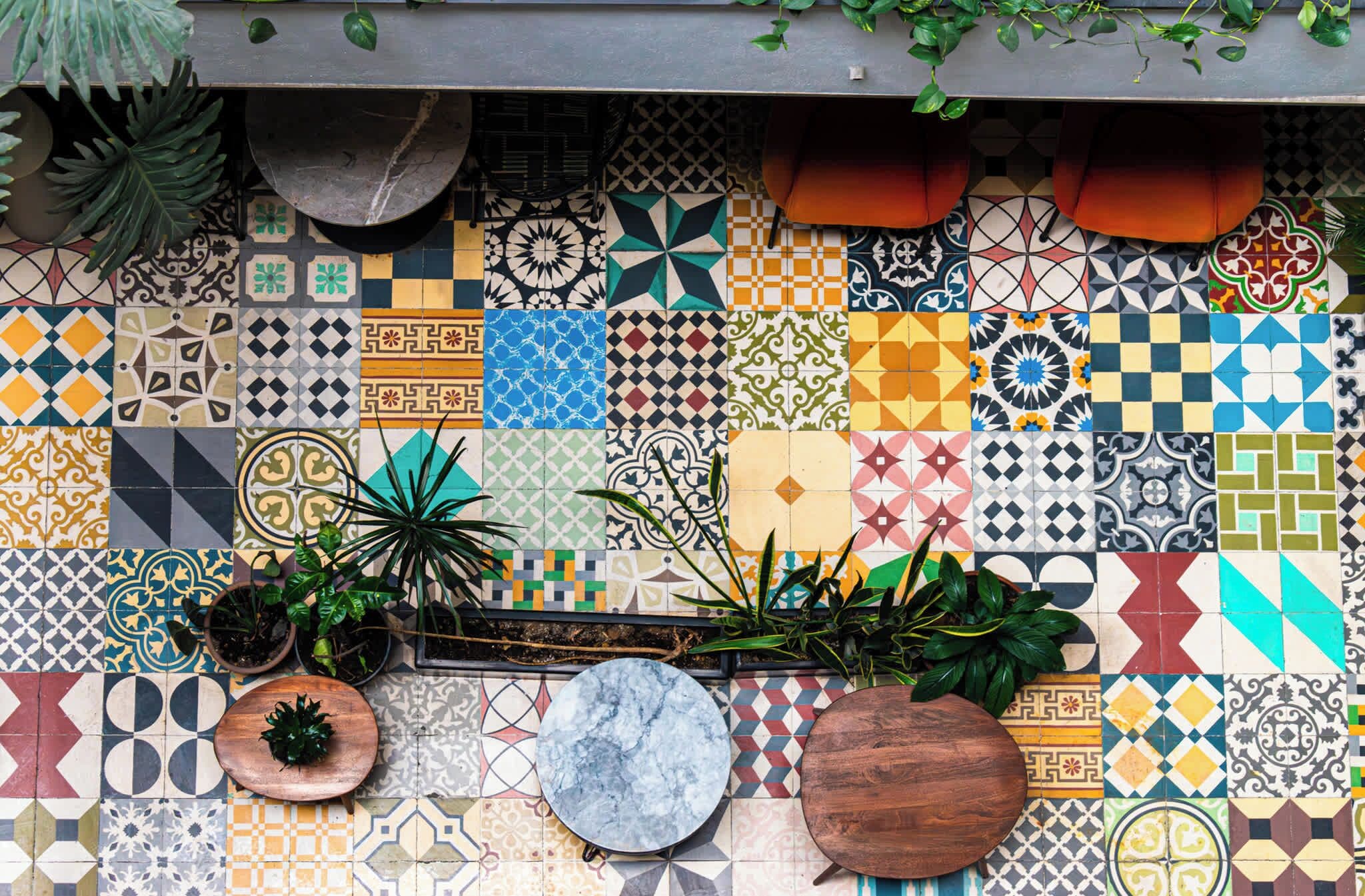Una pared de azulejos con diversos diseños y colores, plantas en macetas y un estante de madera.
