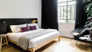 A modern bedroom with a wooden bed, a small stool, a black metal chair, and a large window with black curtains. - Puerta roja Increible ubicacion en condesa suite (Ciudad de México)