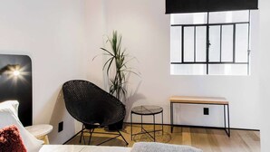 Een moderne kamer met een groot raam, een zwarte stoel, een klein rond tafeltje en een bank.