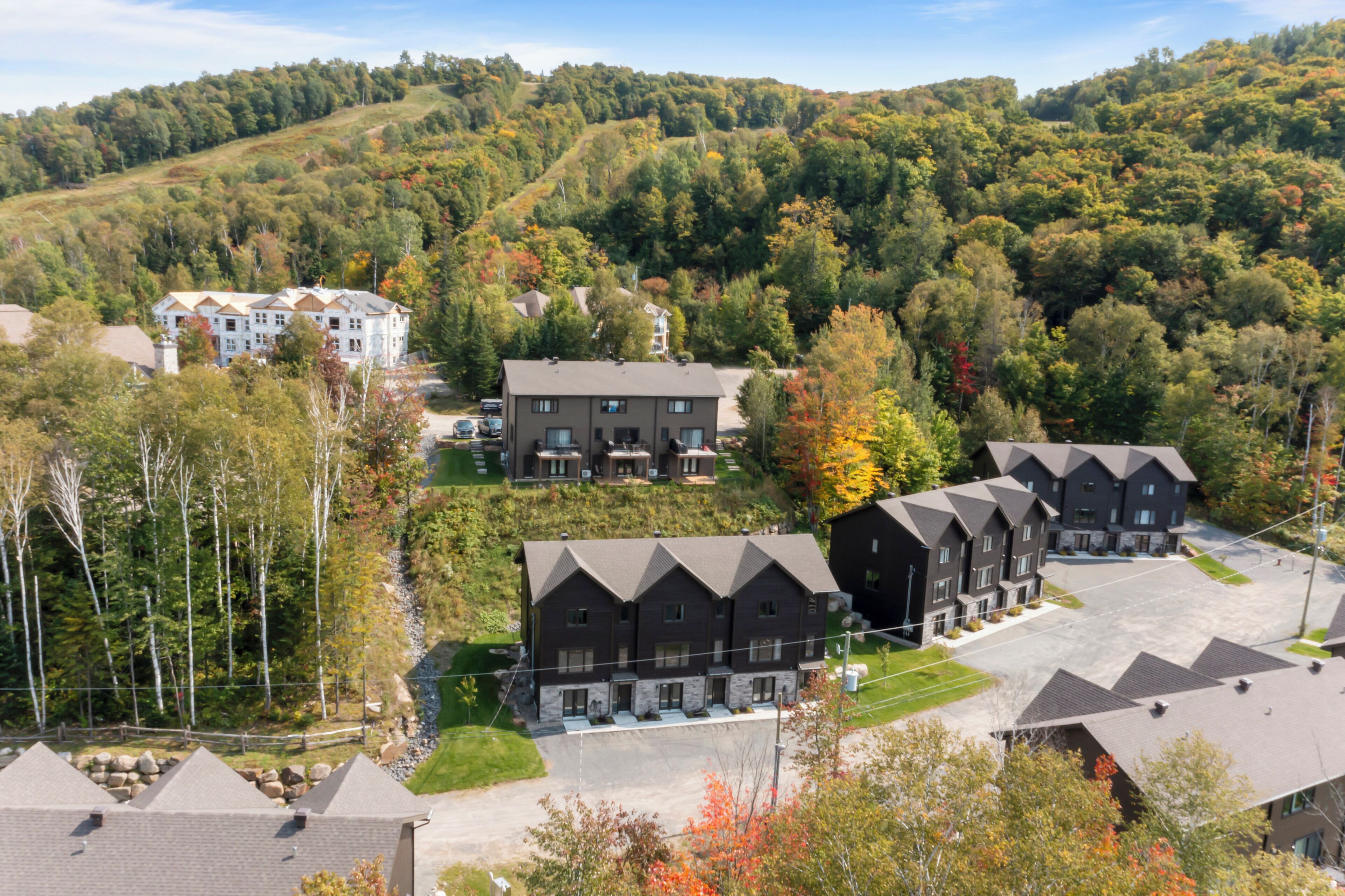 A residential area with multiple two-story houses, a parking lot, and a hilly backdrop with autumn foliage.