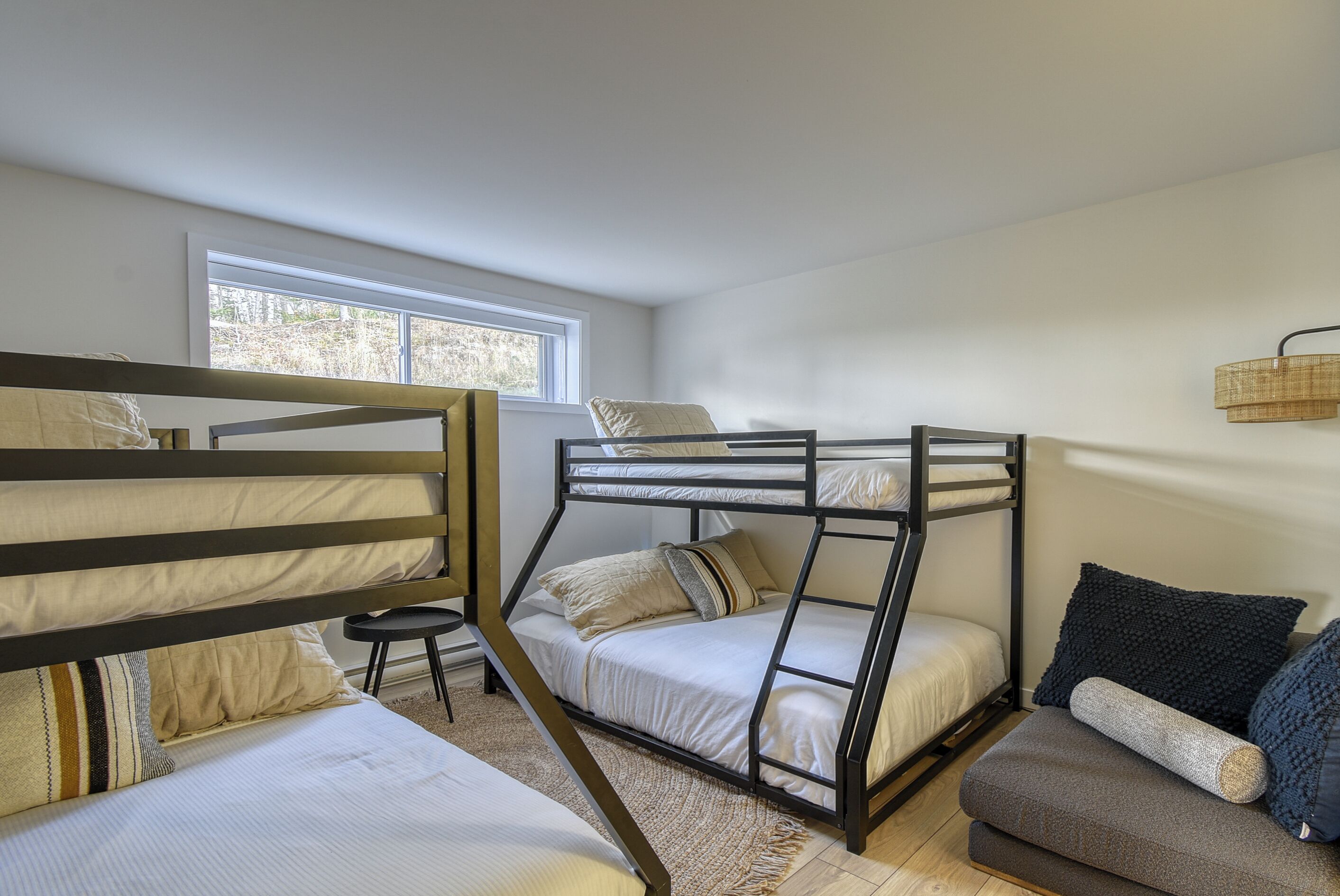 A room with bunk beds, a sofa, and a window providing natural light.