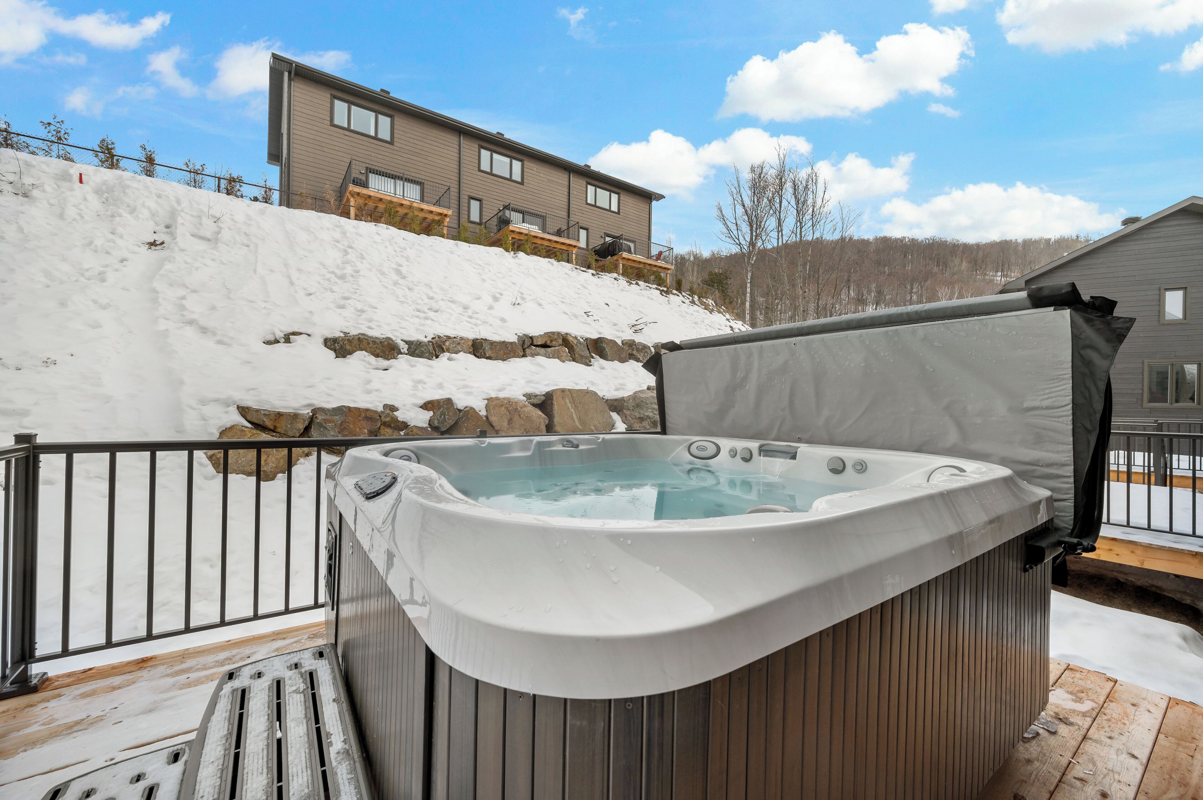 Un bain à remous sur une terrasse en bois, avec un mur en pierre et un bâtiment en arrière-plan.