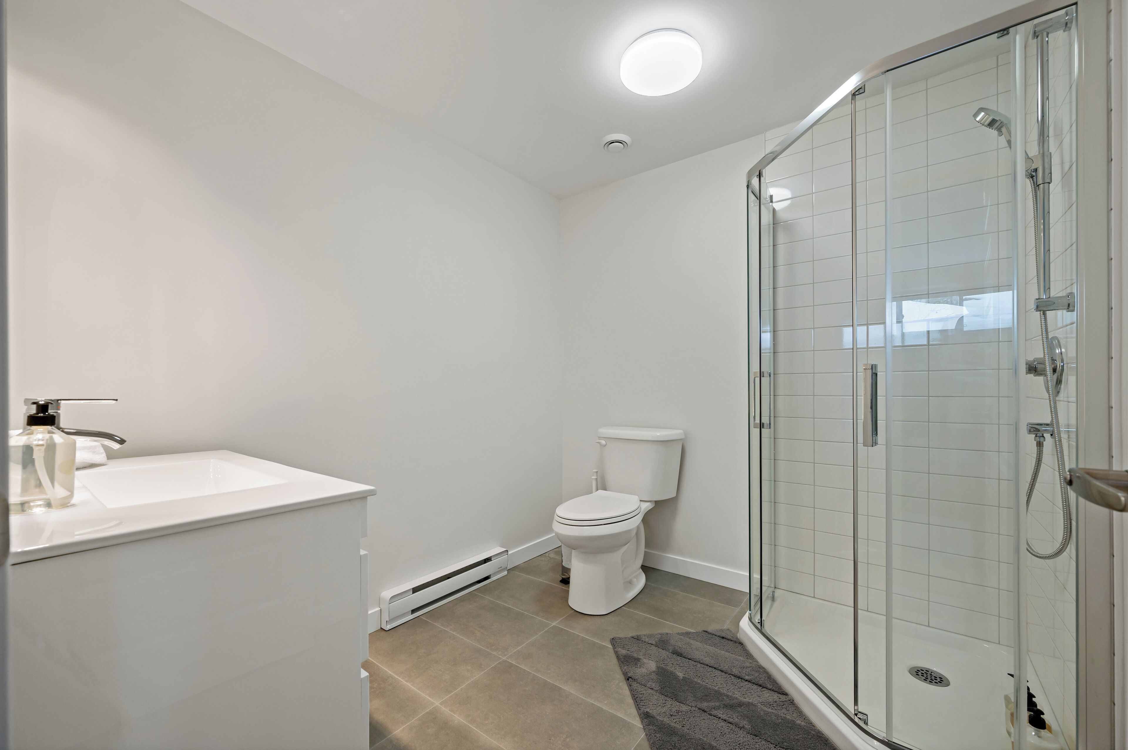 Et moderne badeværelse med en hvid vask, toilet og glasbrusekabine.