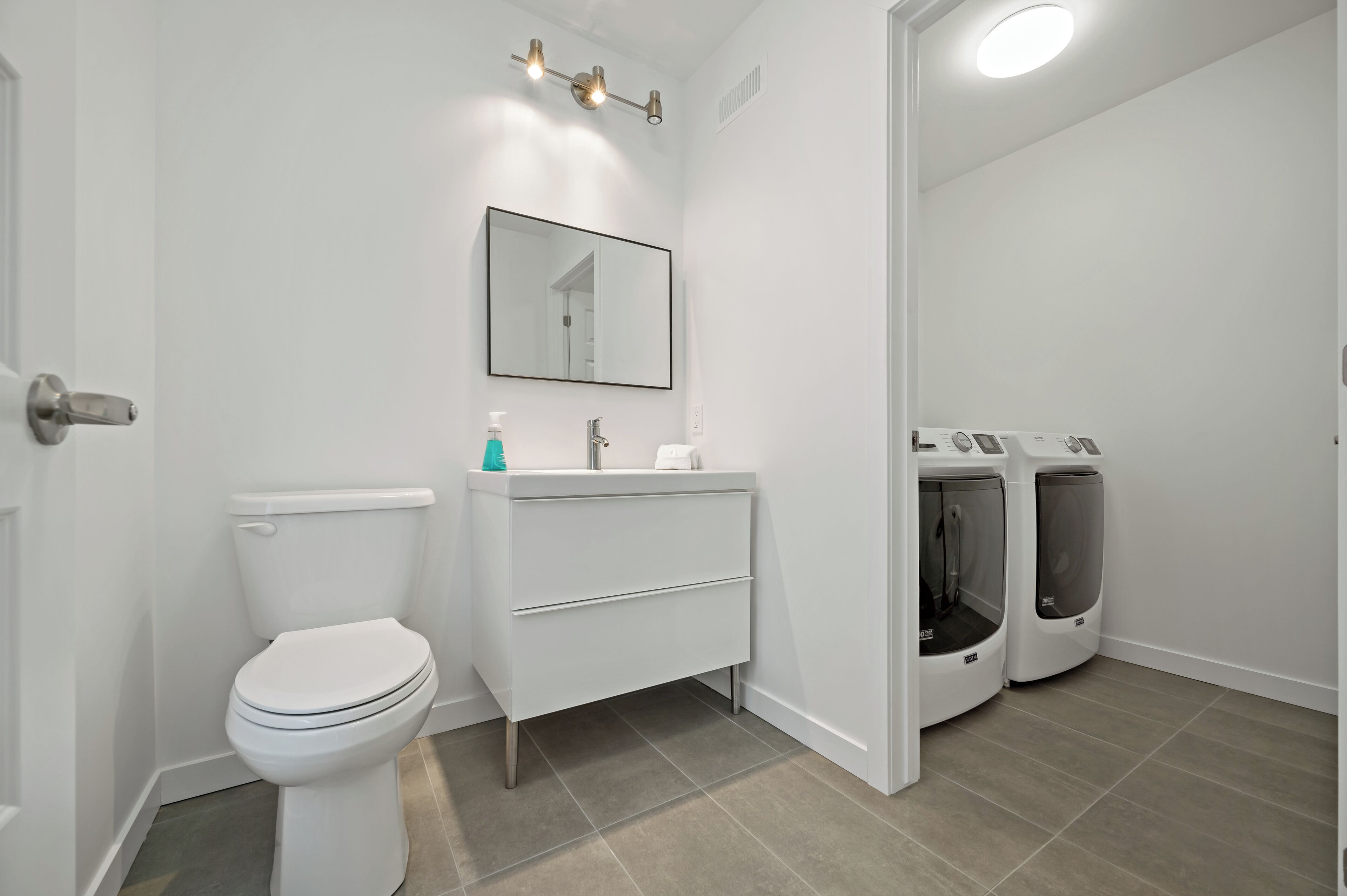 Ein modernes Badezimmer mit Toilette, Waschbecken, Spiegel und zwei wandmontierten Waschmaschinen.
