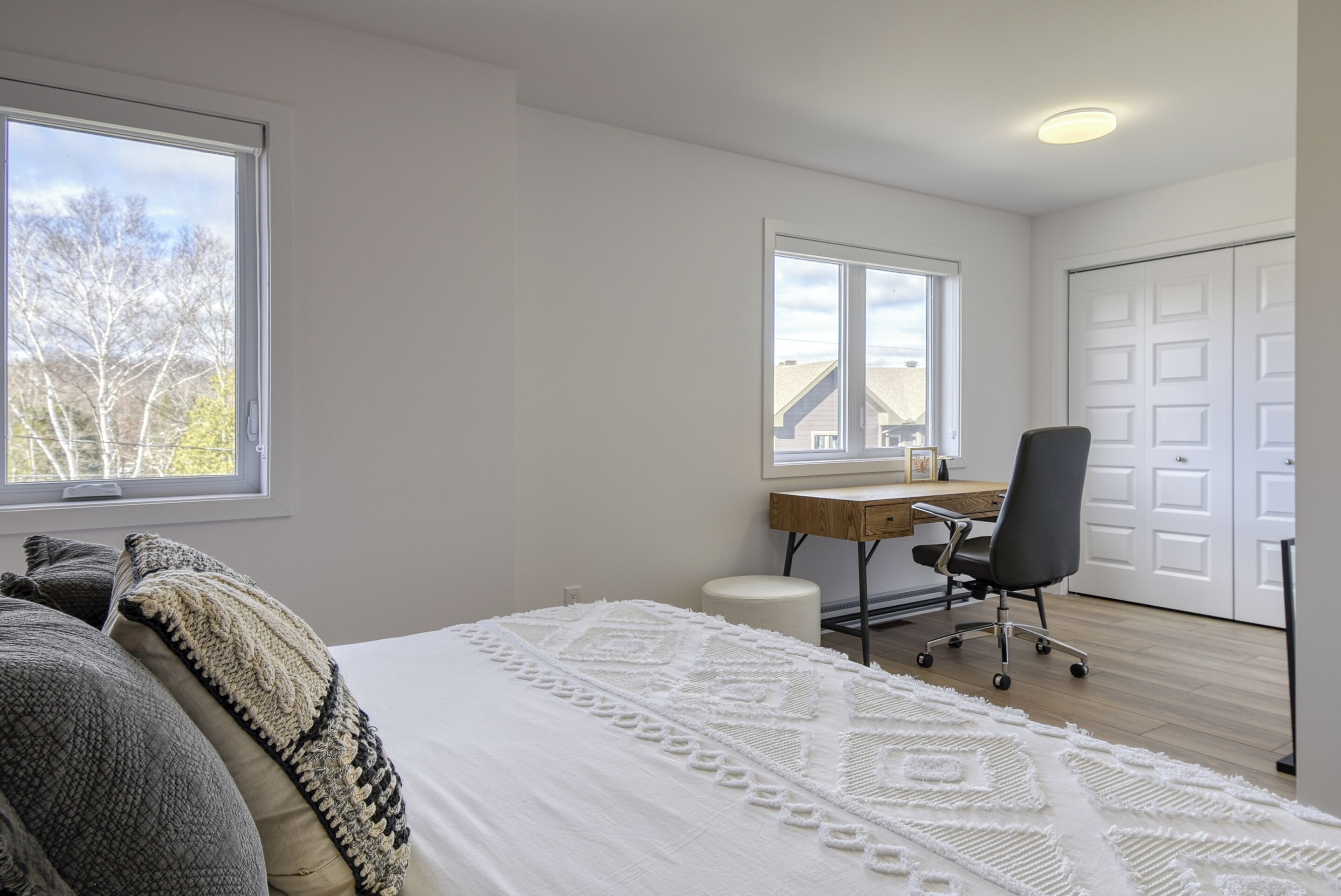 Une chambre à coucher avec un lit, un bureau et une chaise. Il y a une fenêtre et une porte.