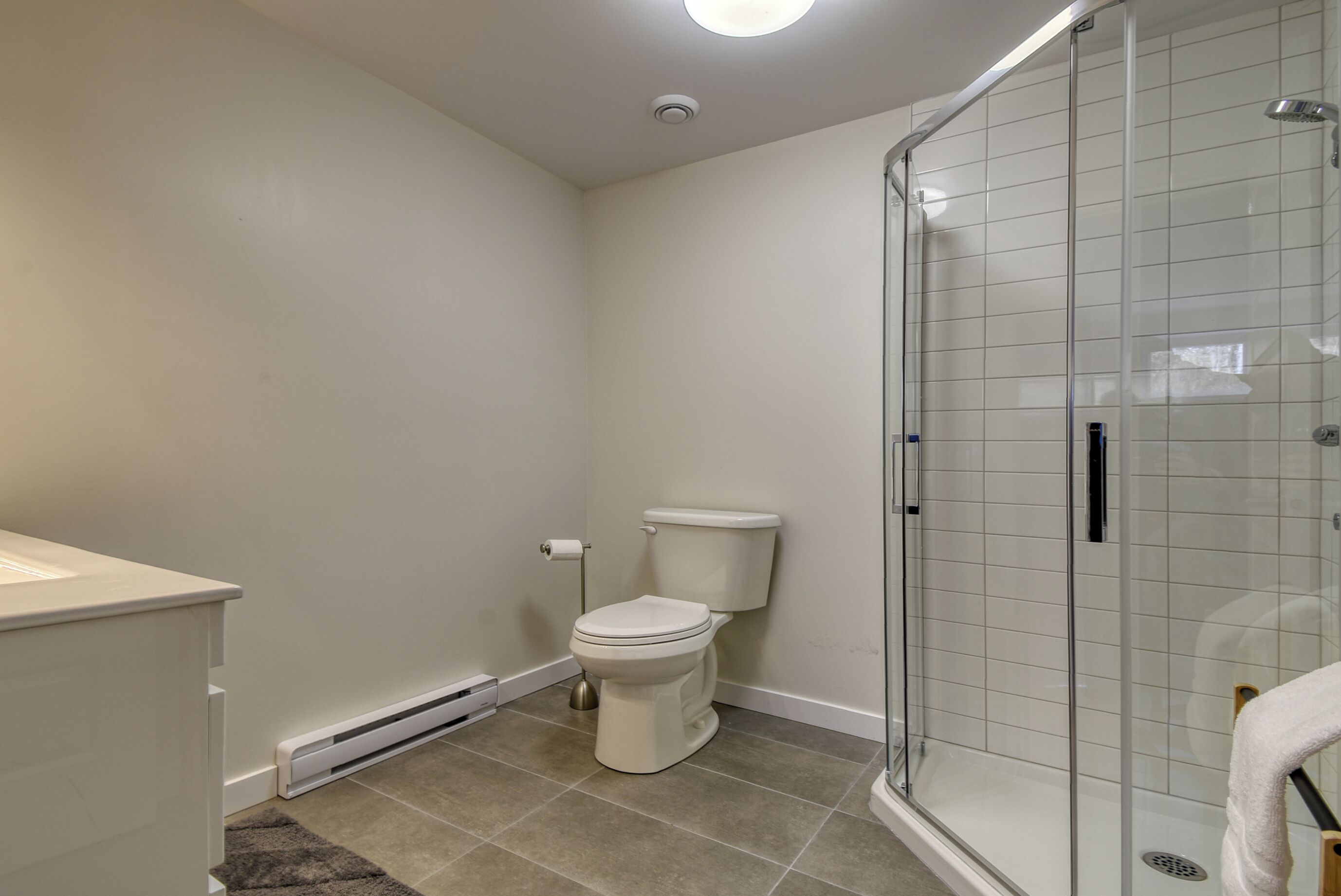 Un baño moderno con inodoro, cabina de ducha de vidrio y lavamanos blanco.