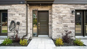 A stone facade with a dark brown door, a number '72' sign, and a garden with small plants. - Le Relais Mont-Blanc (Les Laurentides)